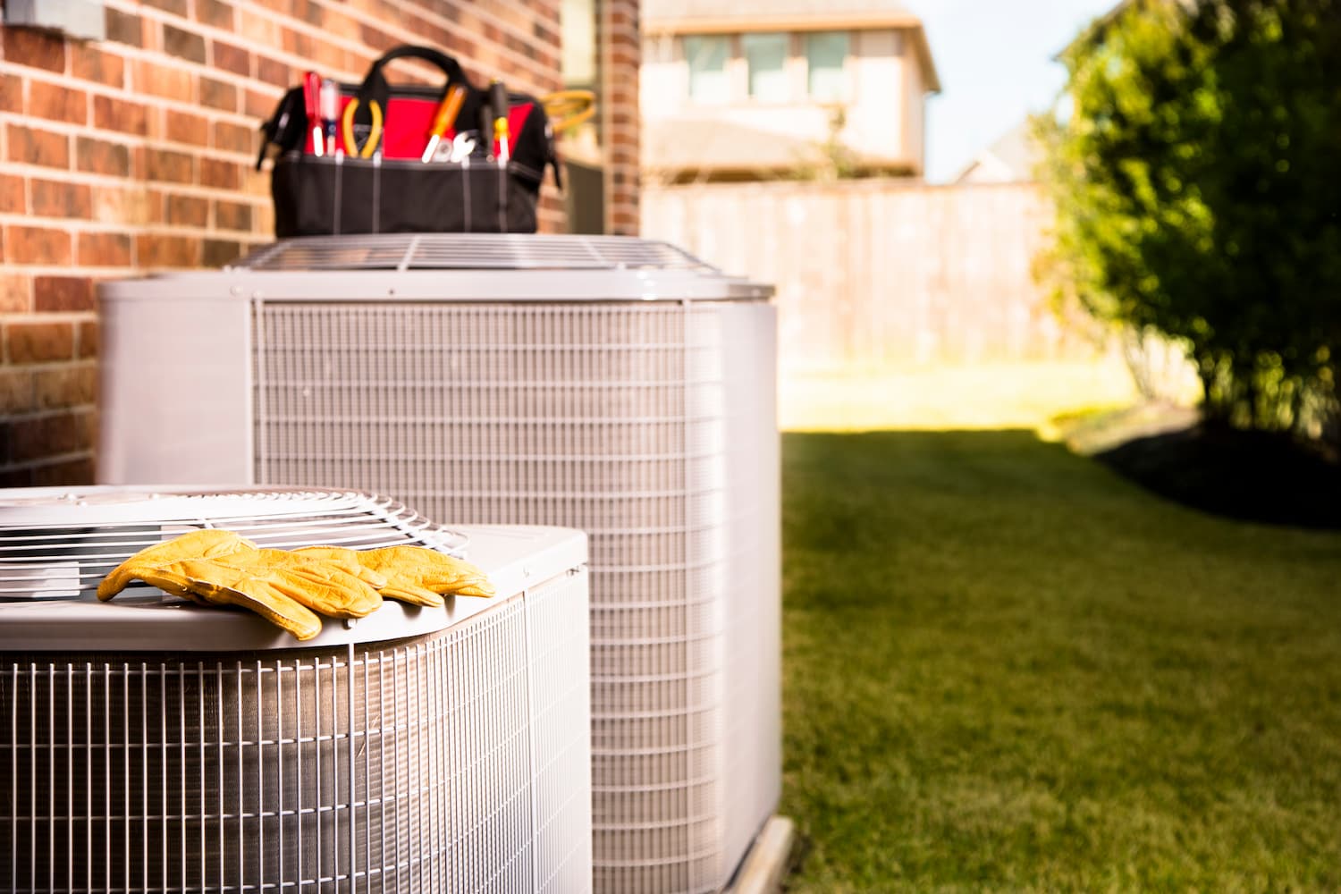 Outdoor air conditioner unit with gloves and a tool box resting on top of the unit.